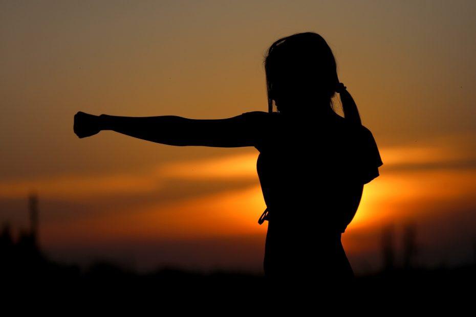 Karate: mulher praticando enquanto o sol se põe no fundo.